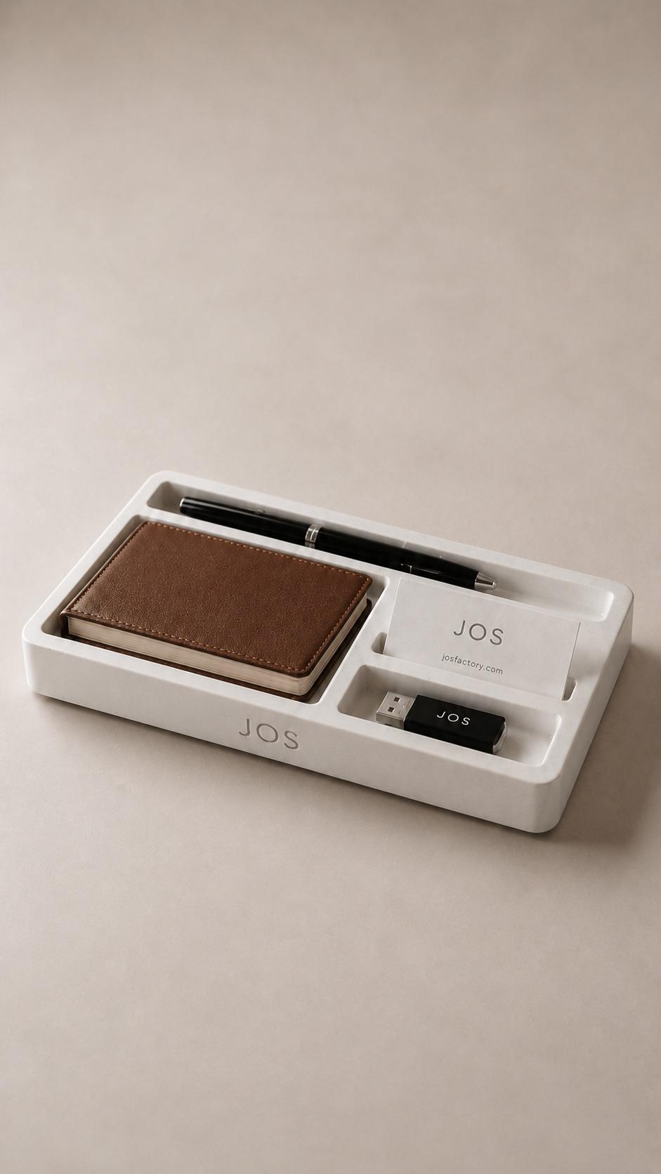 White concrete desk organizer set engraved with the JOS logo, holding a leather wallet, a pen and a branded USB drive