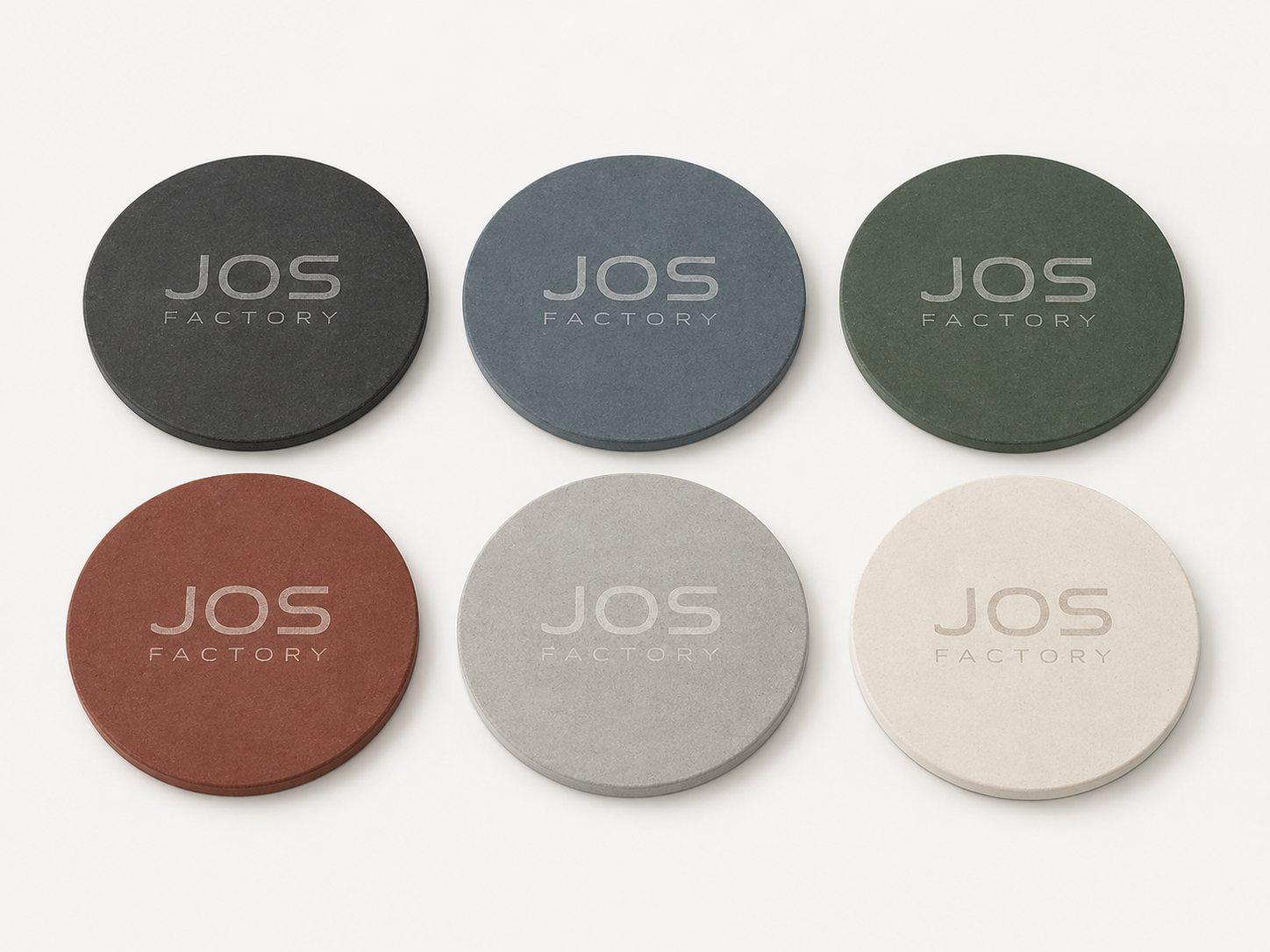 Six round concrete coasters in graphite, blue, green, terracotta, grey and cream, each with an engraved logo